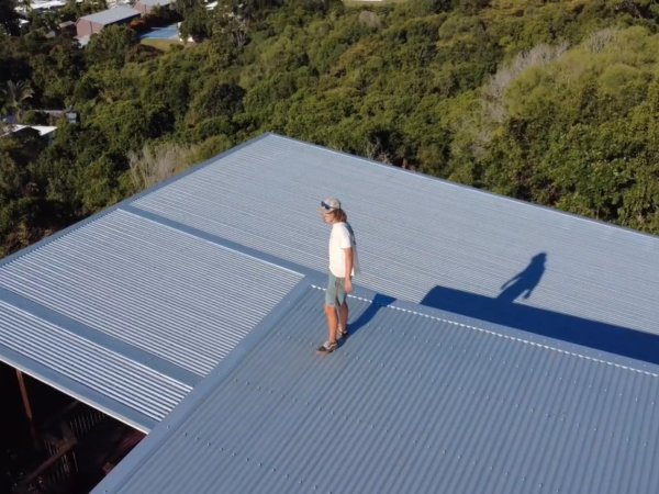 Aerial view of a completed corrugated metal roof above the treeline at Cooee Bay